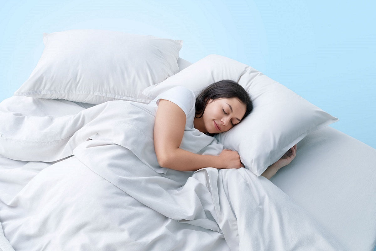A woman sleeping on her side in a bed with clean white linens, set against a light blue background.