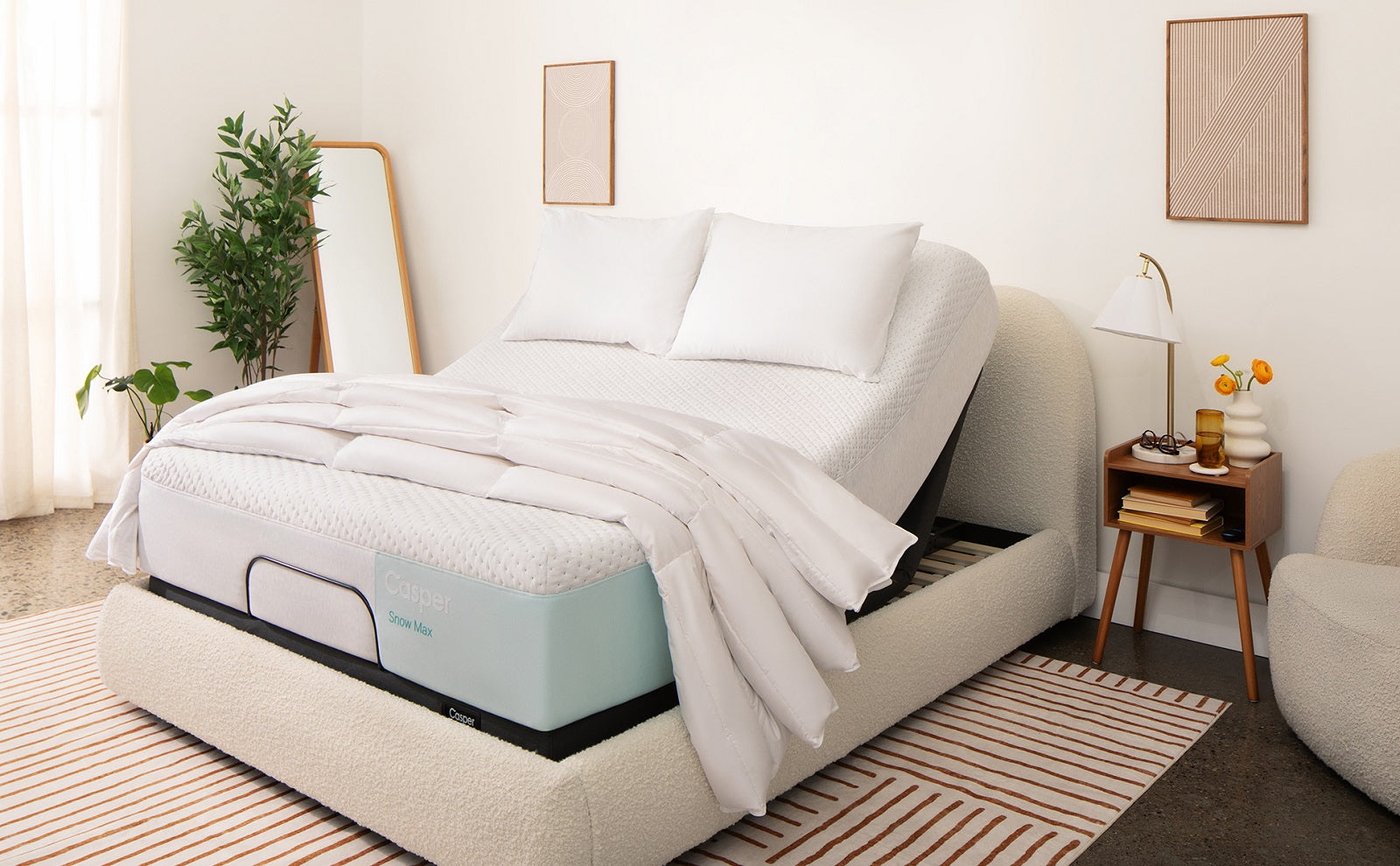 A white Casper Snow Max mattress is shown on an adjustable bed base in a bright, modern room. The bed features a textured cream headboard and frame, set against a striped rug and surrounded by minimalist decor.