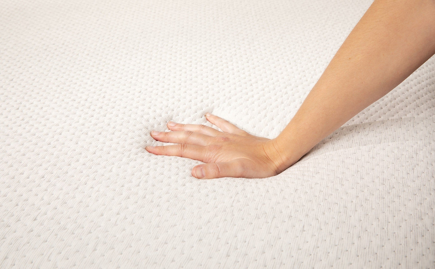 A person's hand pressing down into the soft, textured white surface of a mattress to demonstrate the material's responsiveness and pressure relief.