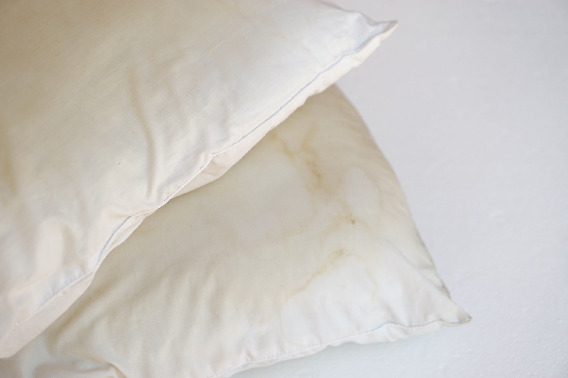 wo white pillows with visible yellow stains on the fabric, placed on a light surface.
