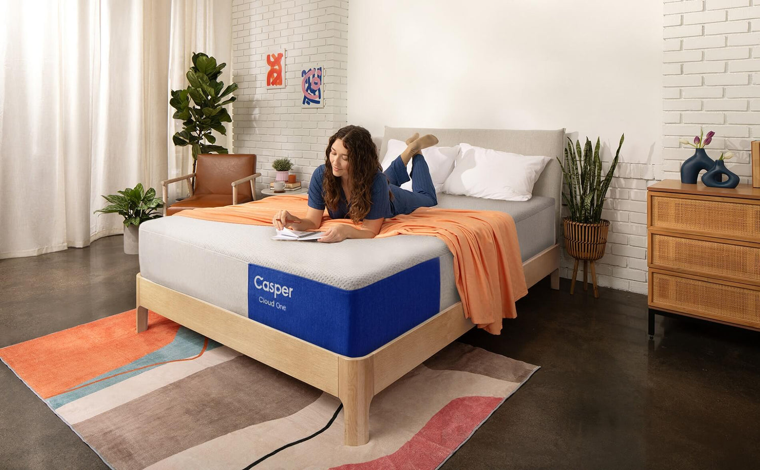 A woman lies on a Casper Cloud One mattress in a modern, sunlit bedroom while writing in a notebook.