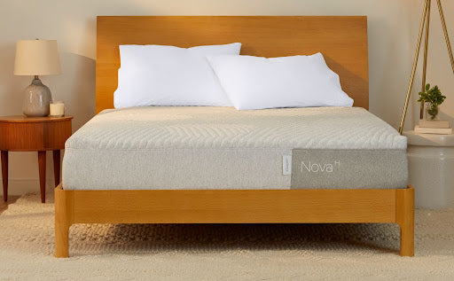 A bed featuring a light-colored Nova Hybrid mattress on a simple, modern wooden bed frame with a matching headboard, flanked by white pillows.
