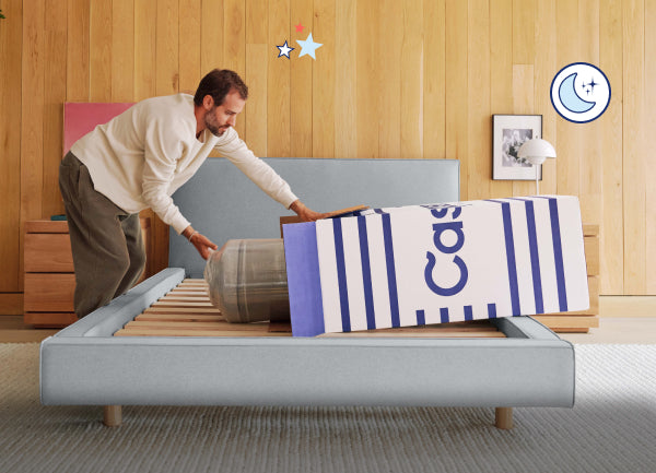 A man unboxes his new Casper mattress over a naked bed frame.