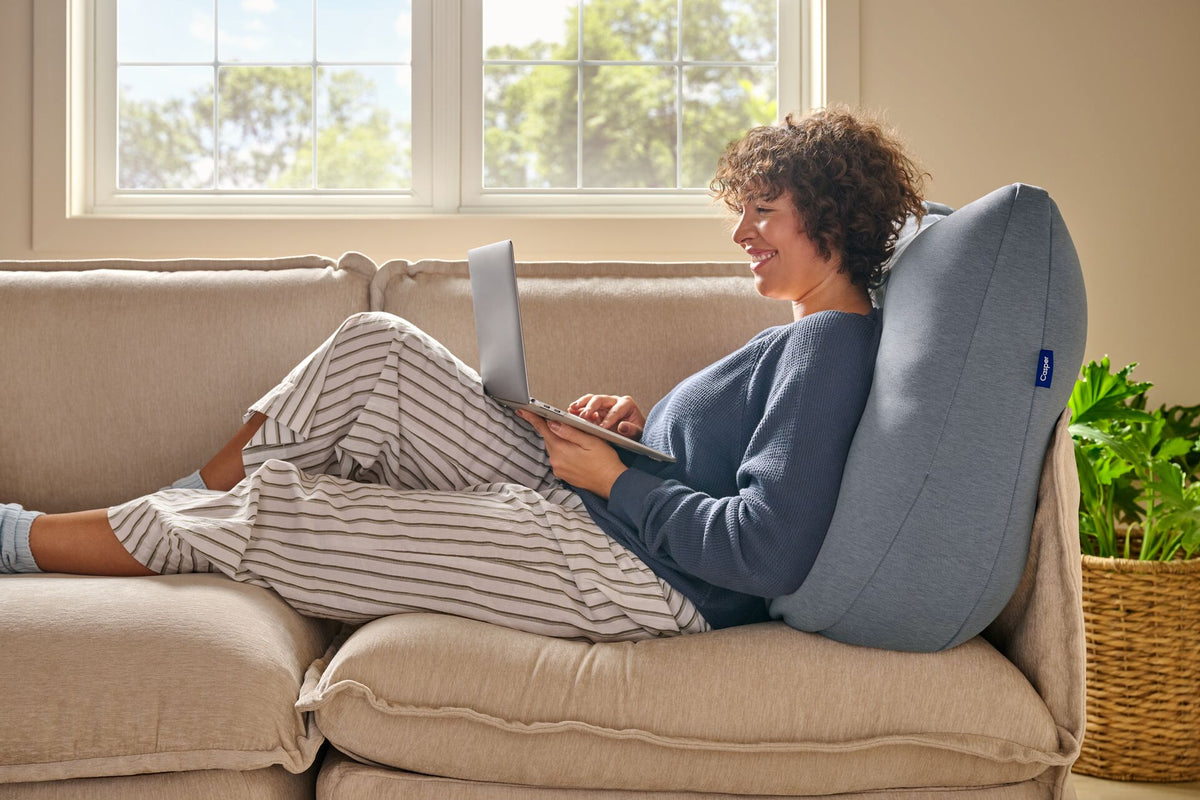 A woman leans back against the Backrest Pillow on a couch.