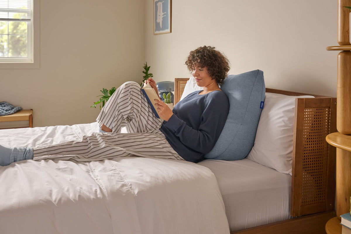 A woman leans back against the Backrest Pillow in bed.
