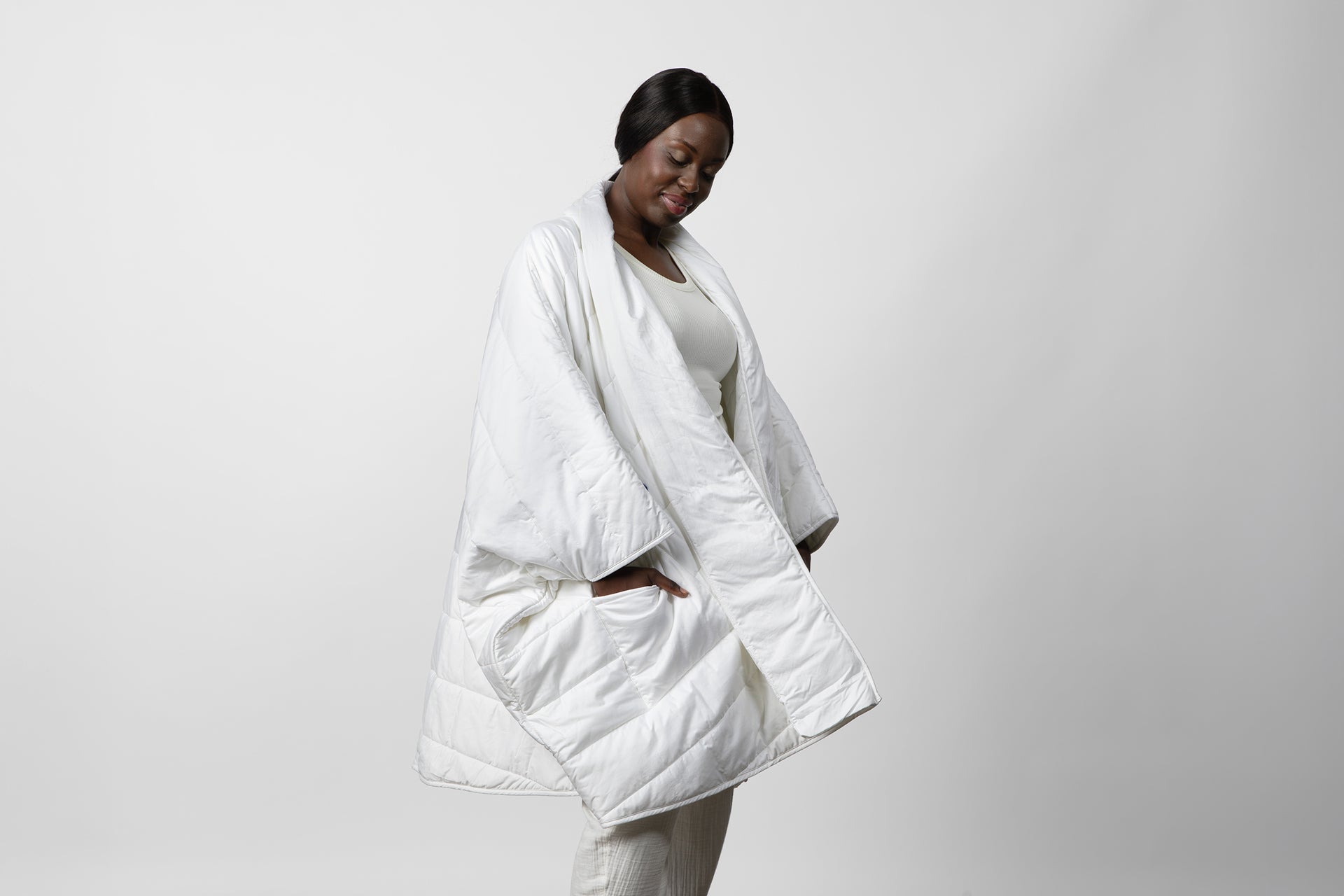 A woman wearing a white Blanket Robe with hands in side pockets, standing against a light background