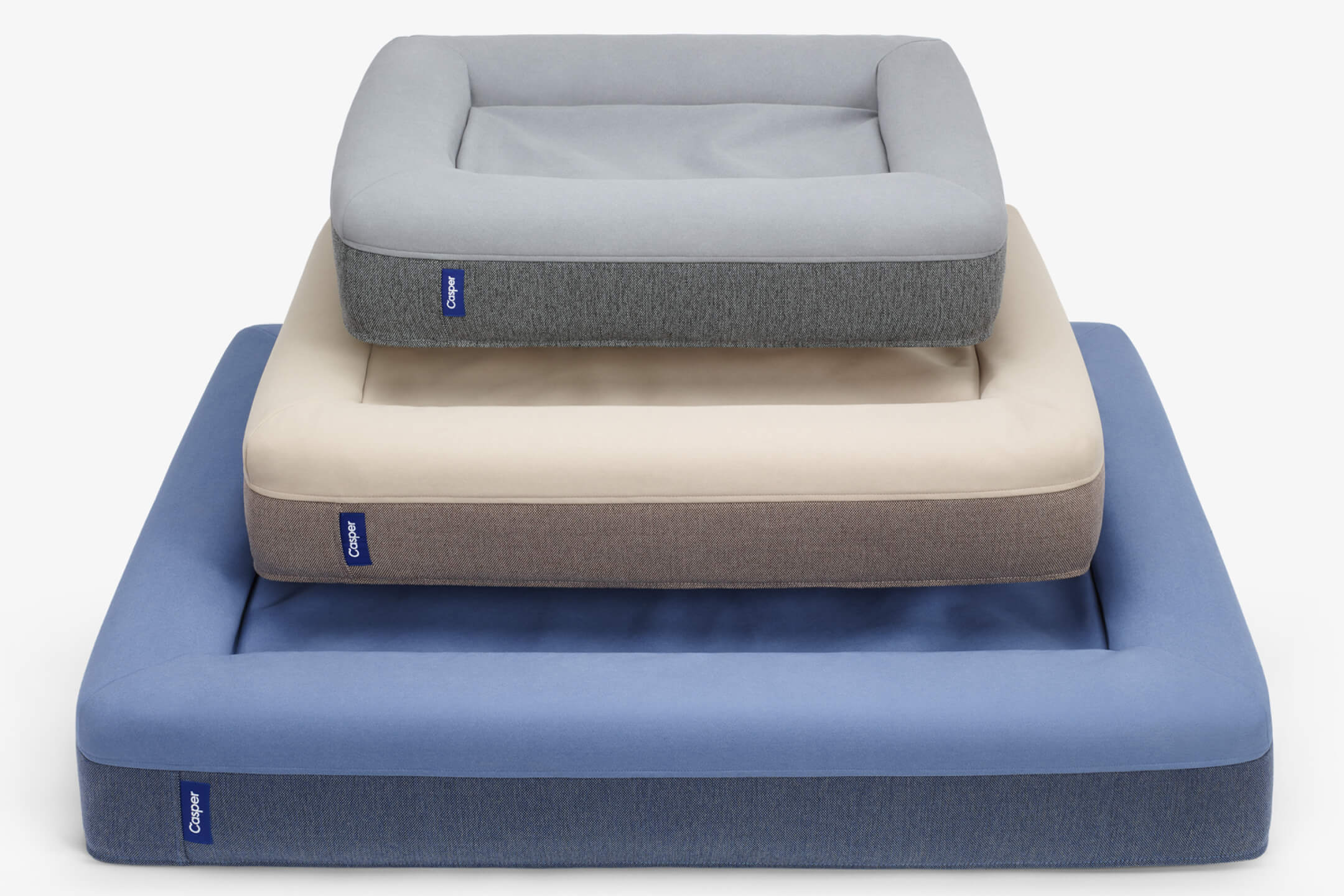 Three sizes of the Dog Bed stacked on top of each other - gray, sand, and blue.
