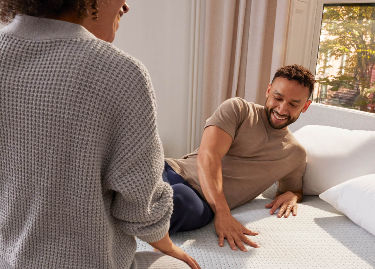 Two people sit happily on their Dream Max mattress and feel how comfortable it is.