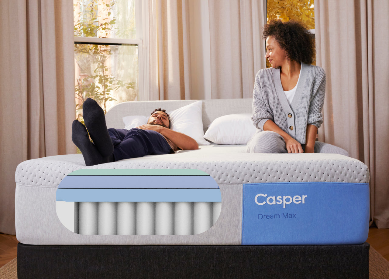Front view of a Casper Dream Max mattress. A couple sits and lies down on the mattress. A graphic is inserted onto the image that shows what the inside of the mattress looks like.