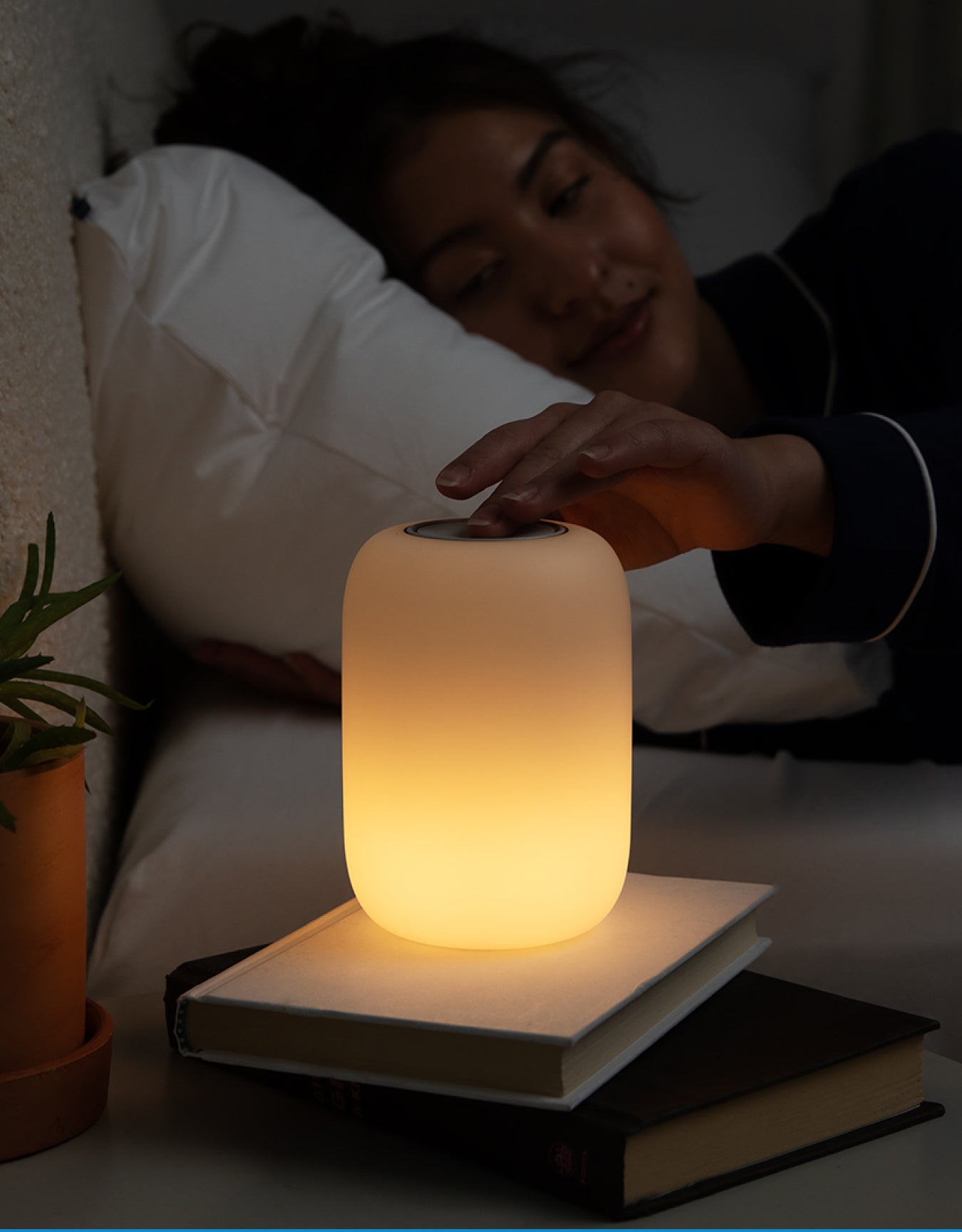 A person lying in bed with a Glow Nightlight on her night stand.