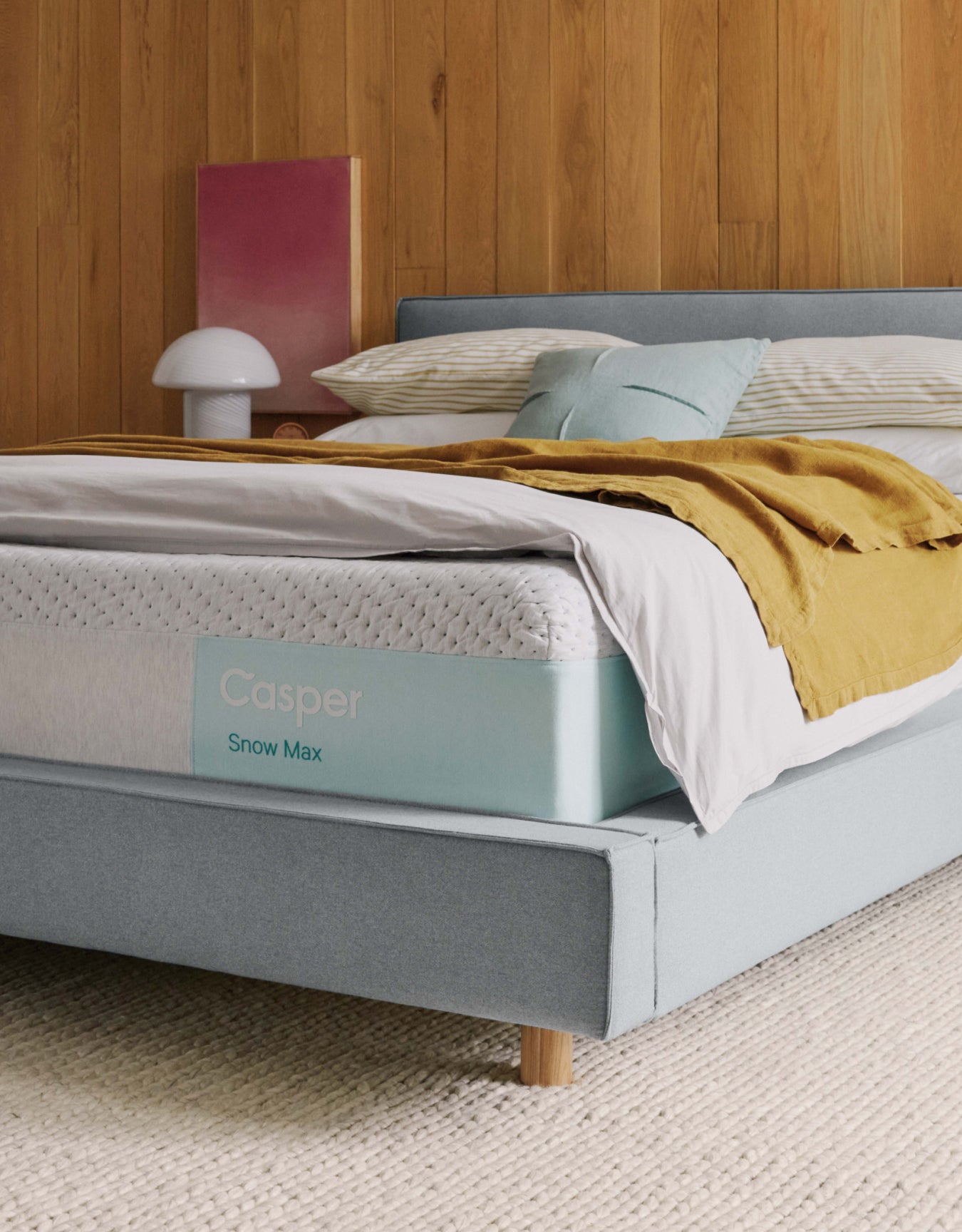 A Casper Snow Max mattress on a bed with pillows and folded blankets on top of it