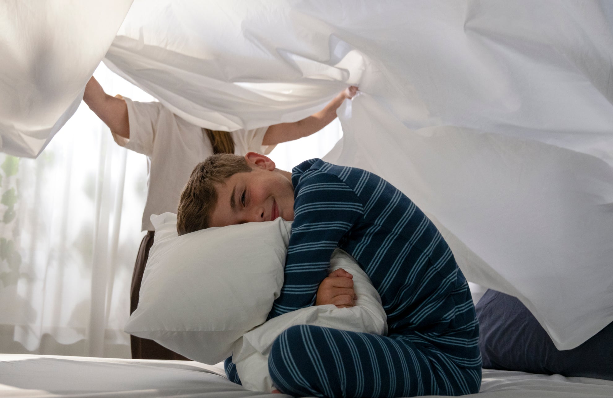 Child playing under a white sheet on a bed