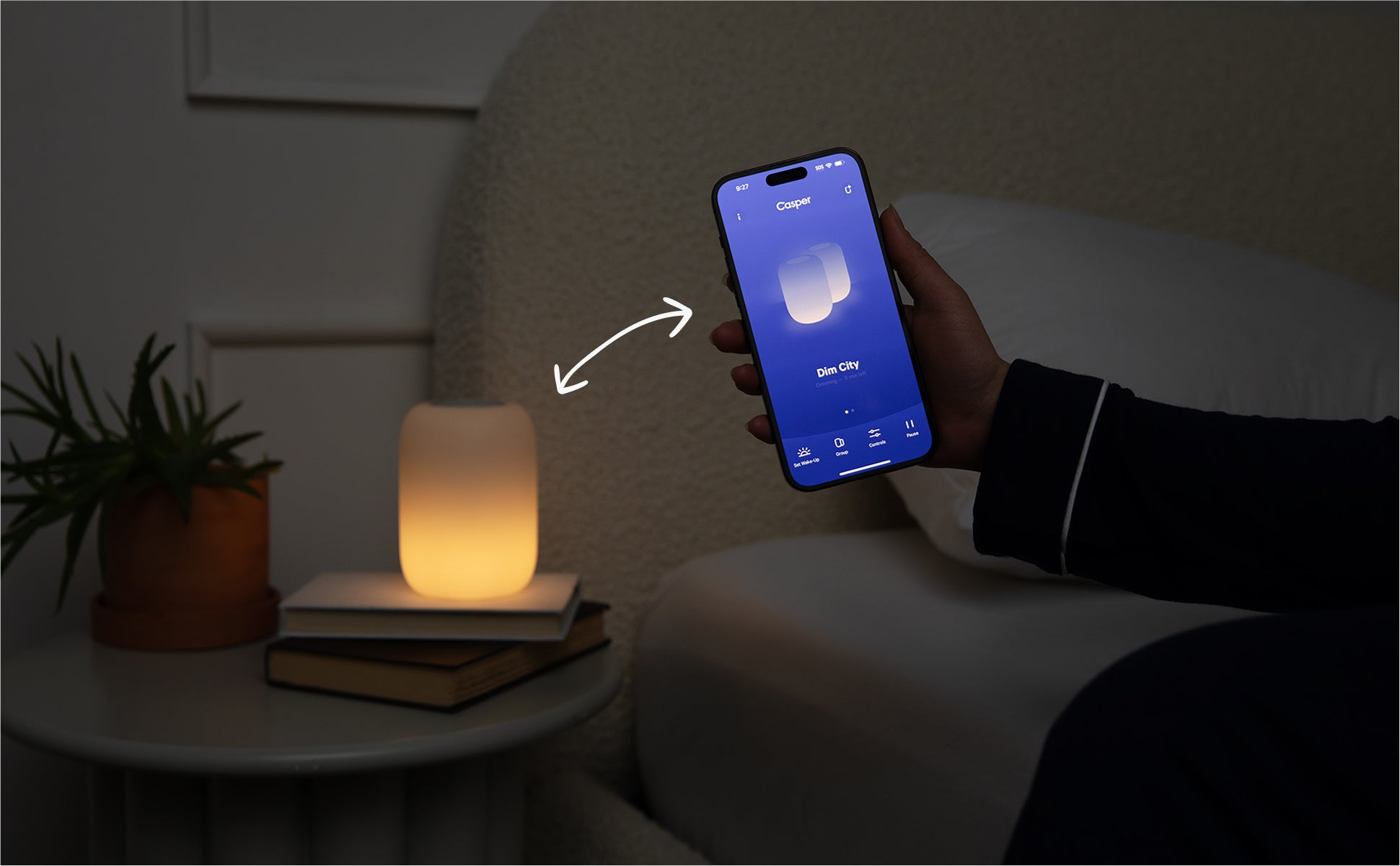 a hand holding a smart phone with the Glow light app open next to a Glow light on a nightstand