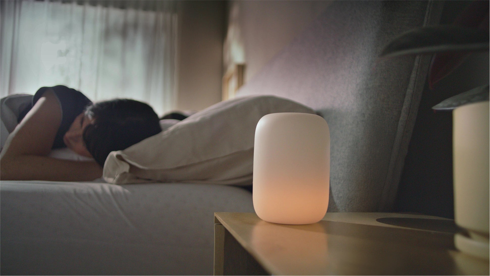 close-up shot of a Glow light on a nightstand with someone sleeping in bed behind it