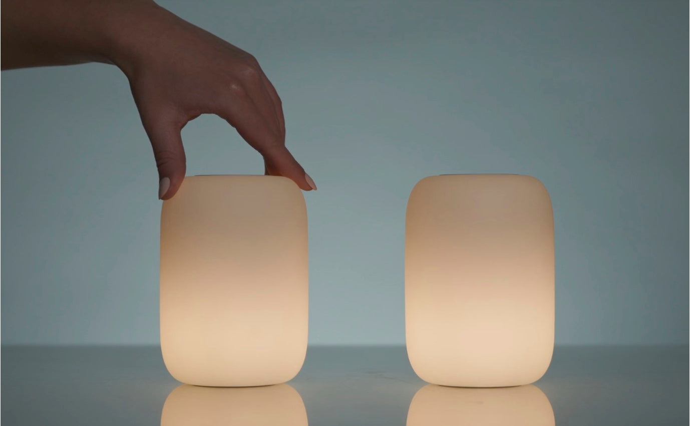 Image of two Glow Lights next to each other, both activated. A person's hand is holding the top of one of them, as if to twist it to turn it off or back on.