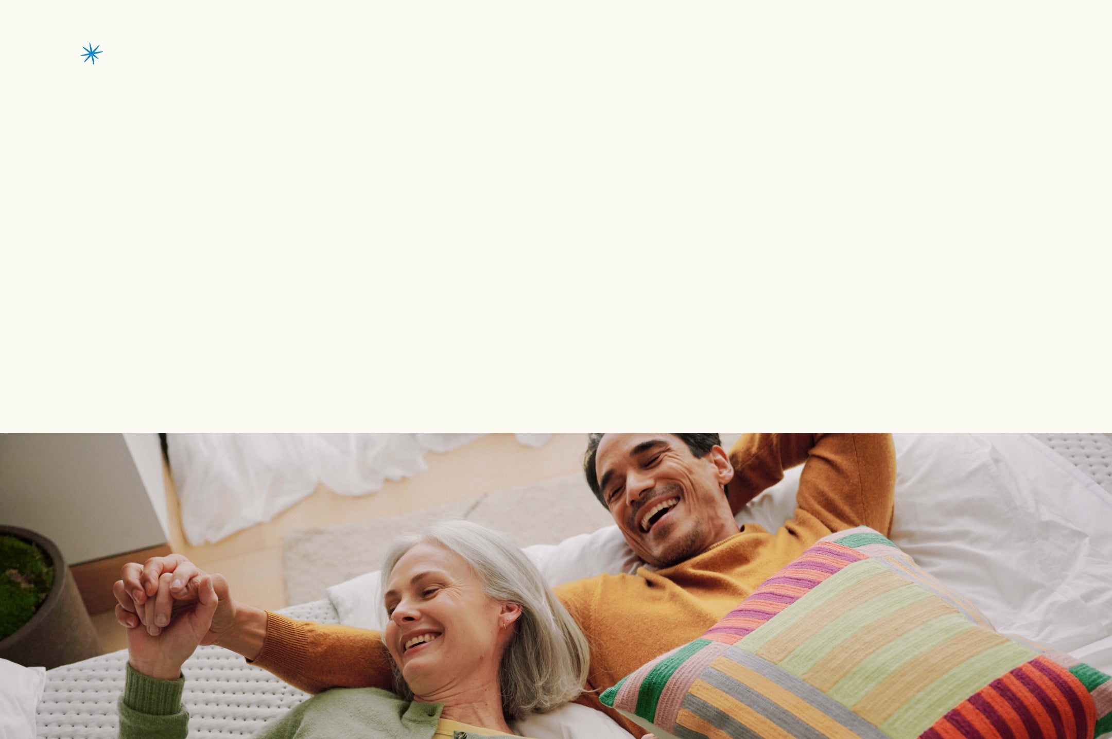 Man and woman lying on a bed holding hands, smiling.