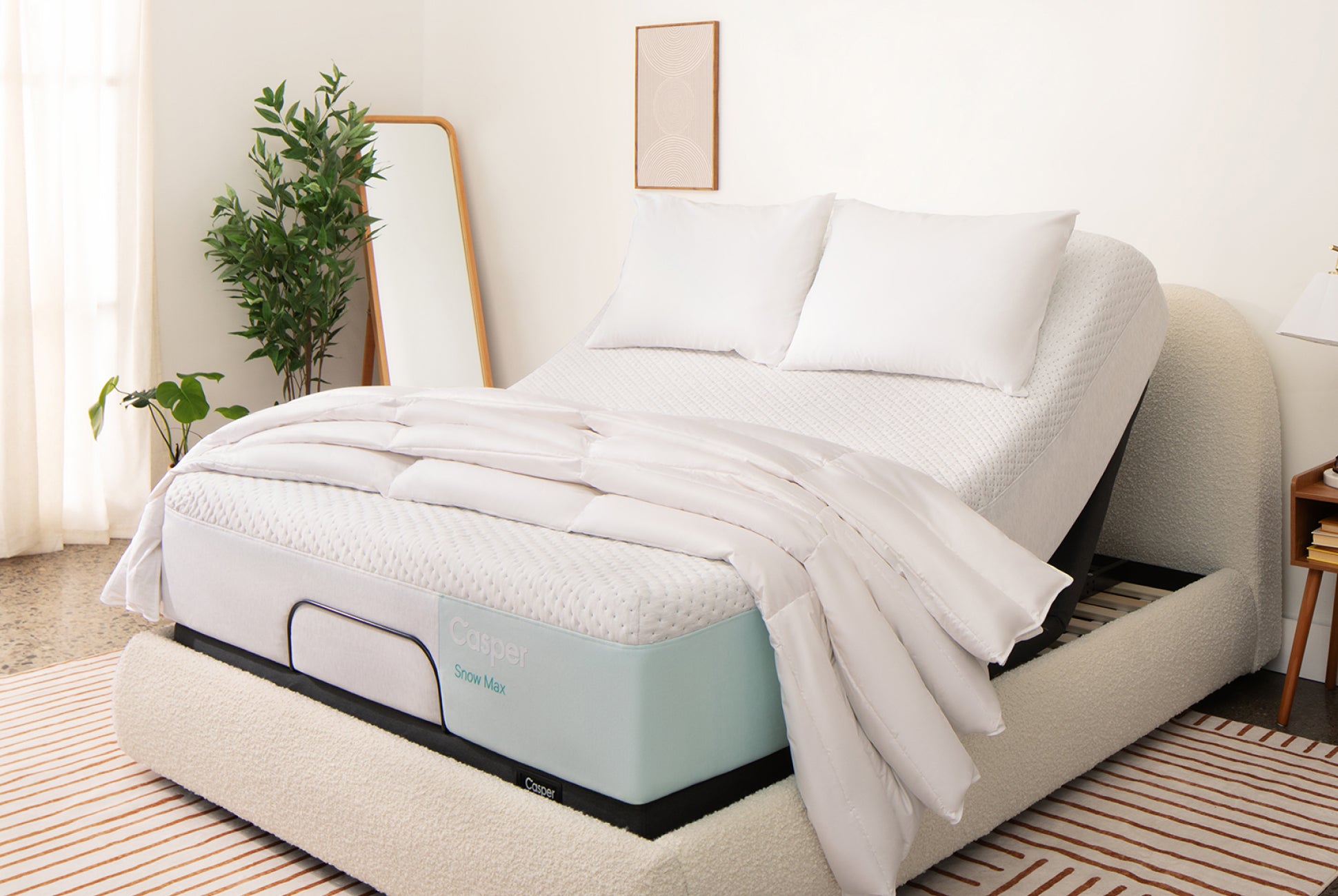 Image of an Adjustable Base Max with a mattress on top of it. The head of the base is raised, lifting up the head of the mattress for you to be lying upright in your bed. The mattress has two pillows and a folded blanket on top of it.