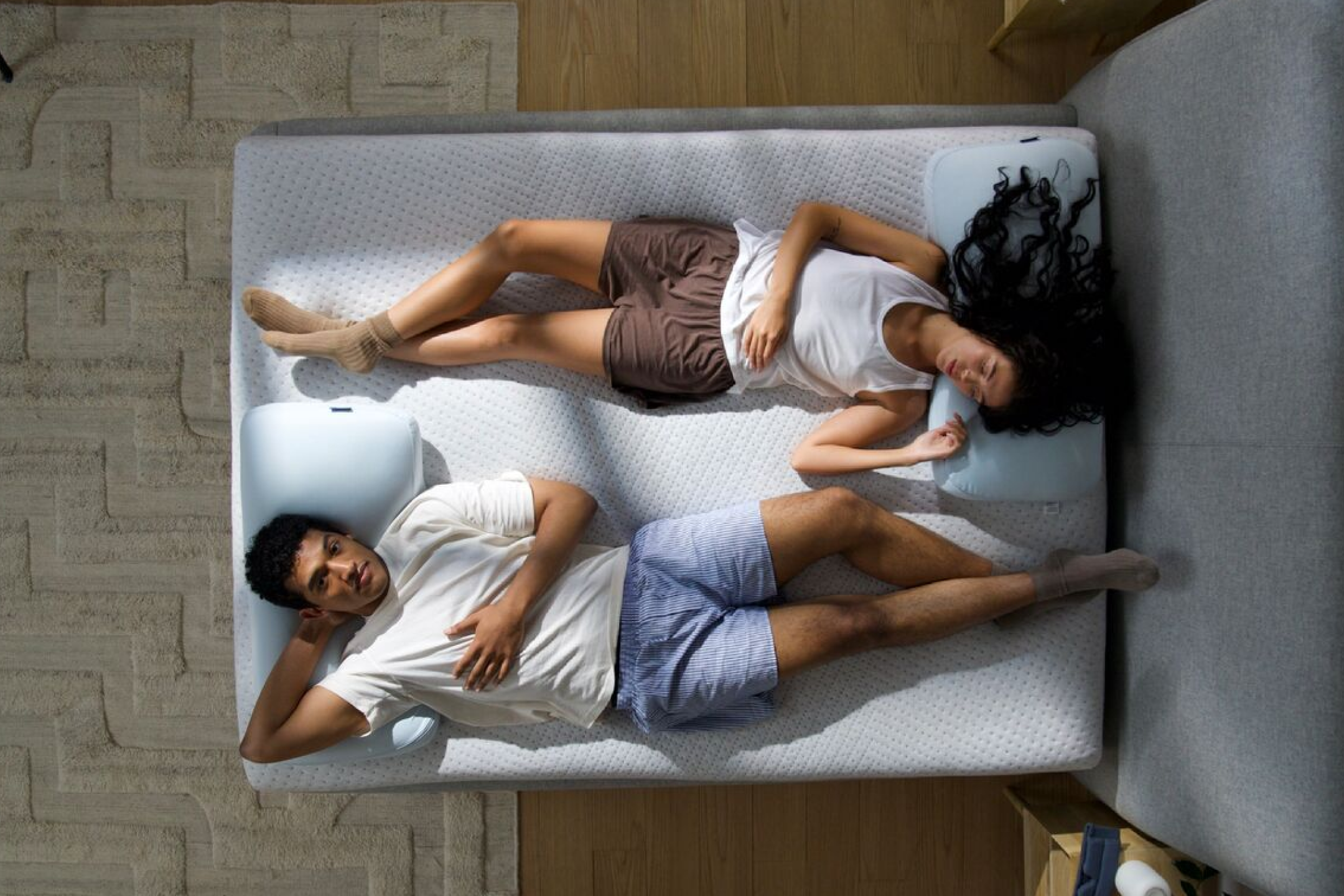 Aerial image of two people lying on their backs on the bed, each one facing a different direction.