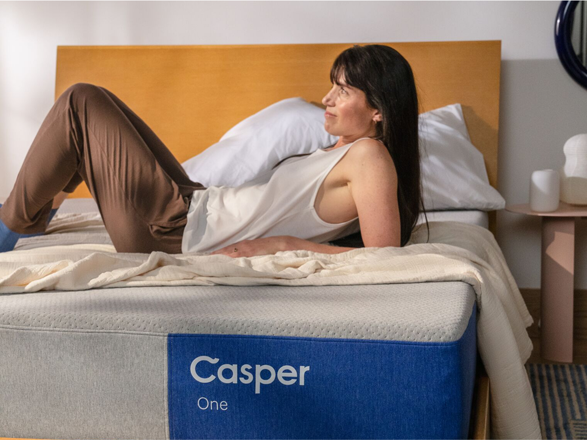 Image taken from the front of a mattress of a woman sitting on a Casper One mattress, leaning back on her elbows.