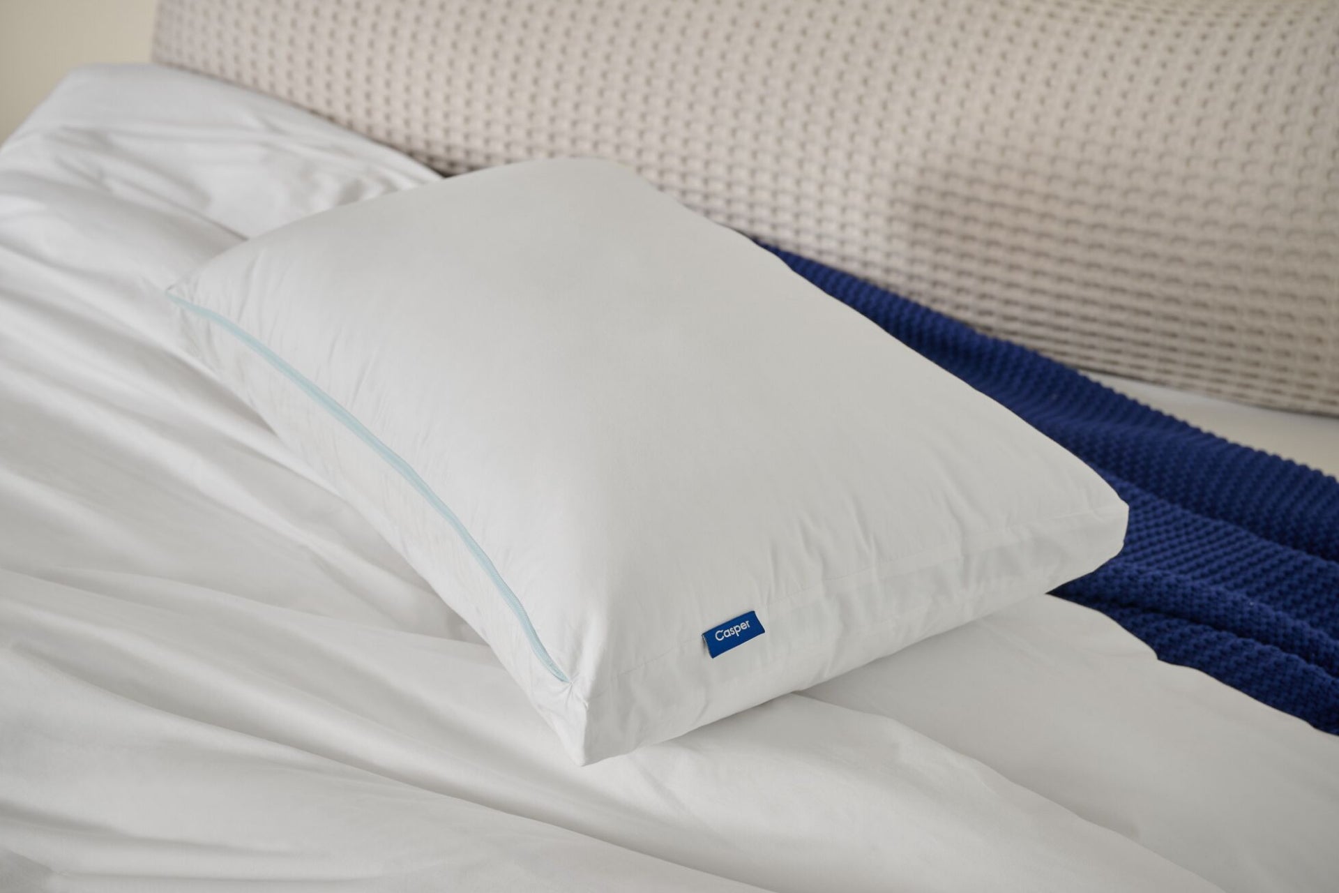 White pillow with a Casper brand logo on a bed over a blanket