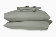 Folded sheets on top of two stacked pillows in pillowcases. Eucalyptus-green colorway.