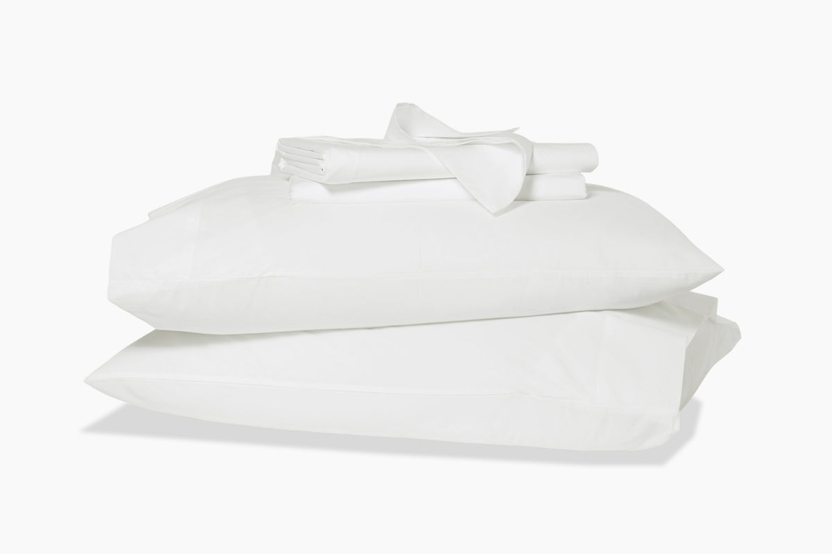 Folded sheets on top of two stacked pillows in pillowcases. White colorway.
