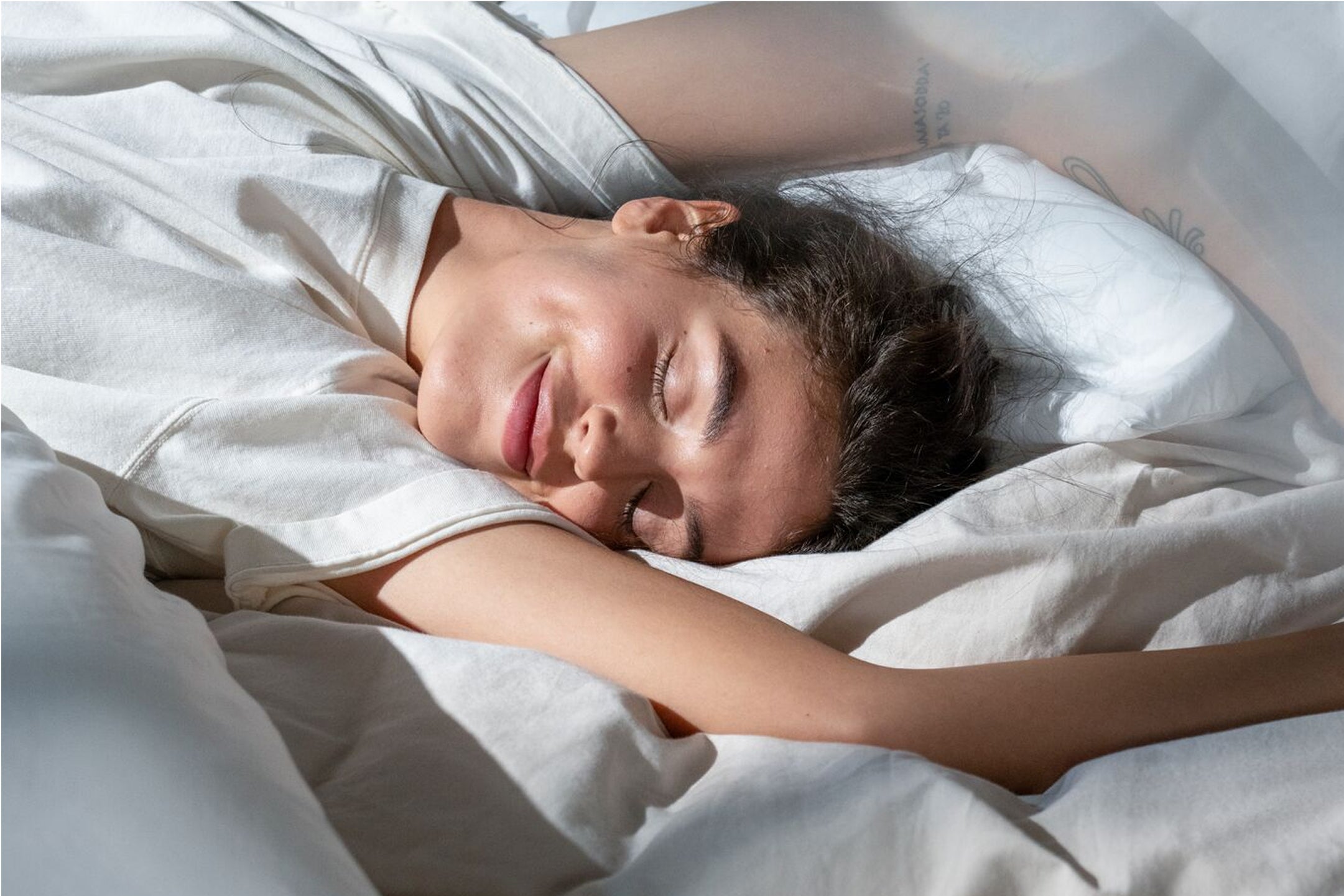 Close-up image of a person lying cozy on their back and smiling on a made bed.