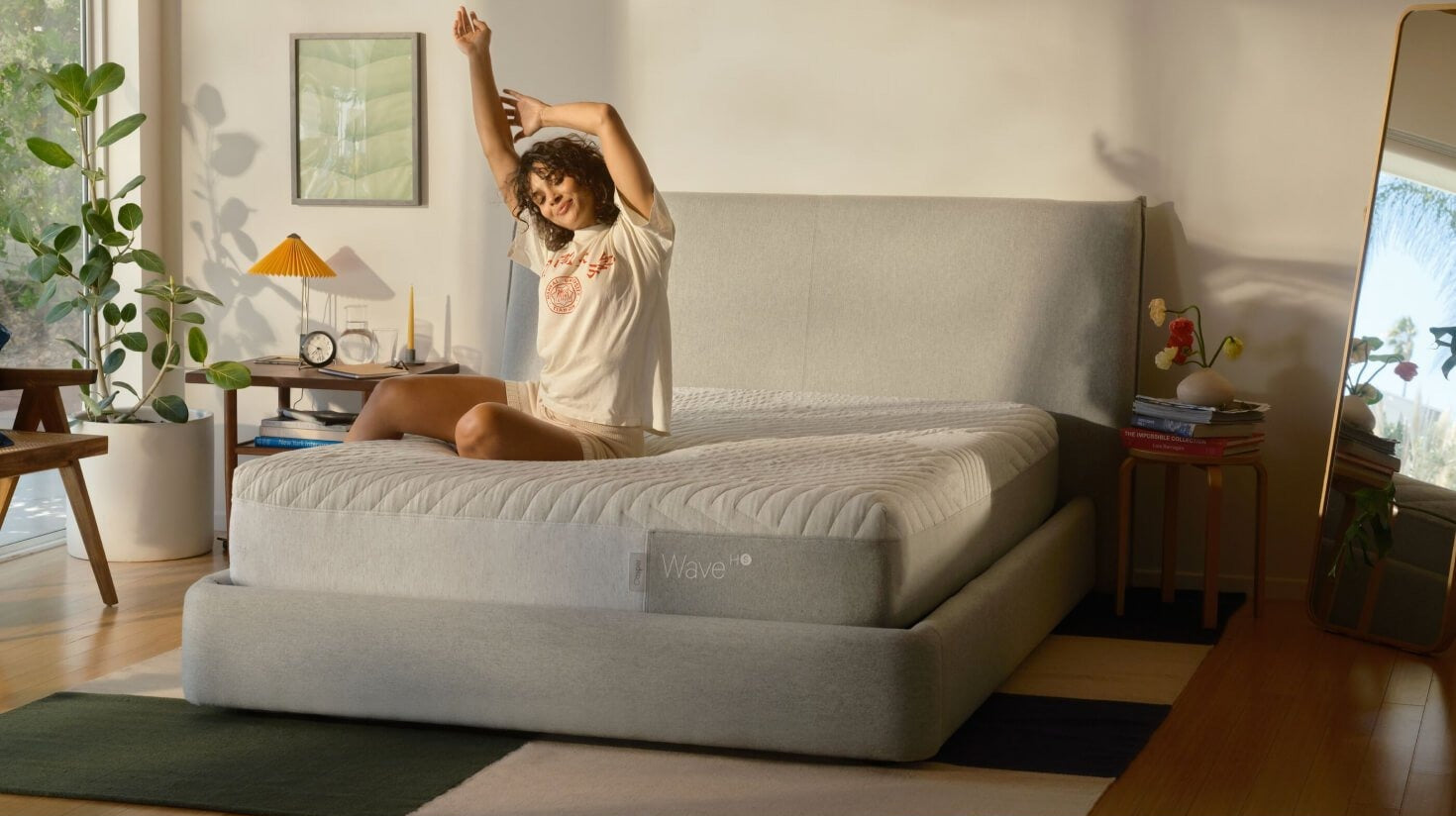 A woman sits on her mattress on top of the Haven Bed Frame