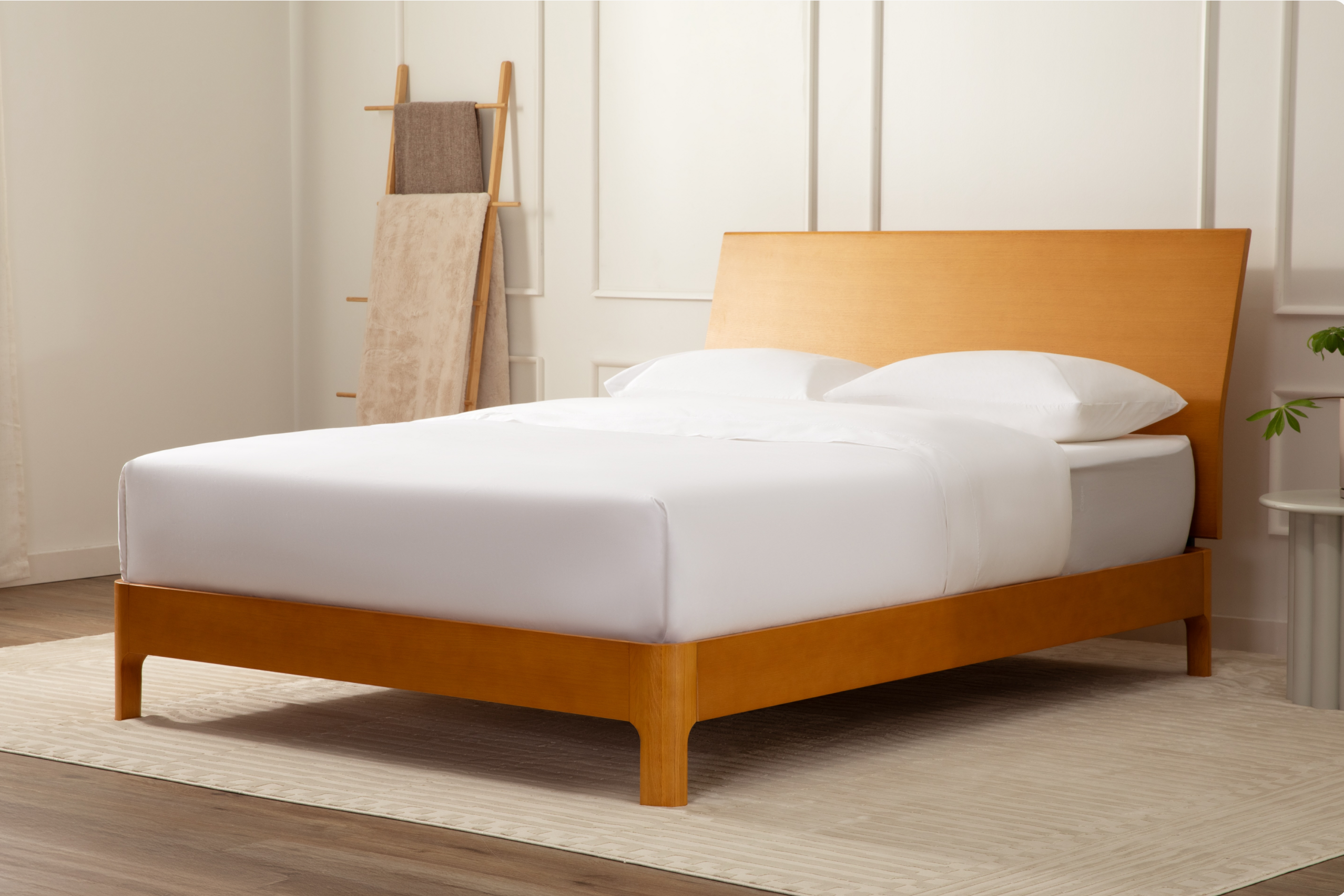 A modern wooden bed frame with a tall rectangular headboard and low footboard, dressed in white bedding and pillows, shown in a bright, neutral bedroom setting.