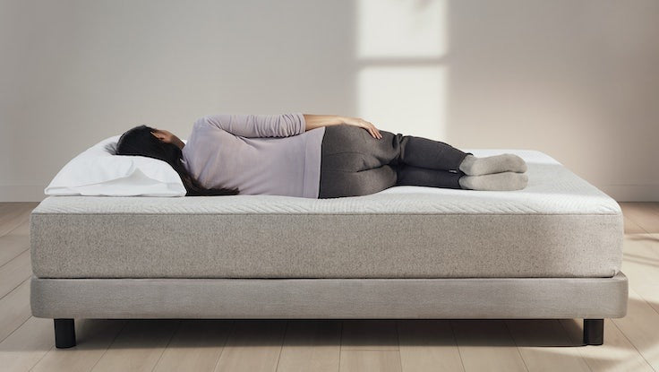 A woman lies on her side on a mattress.