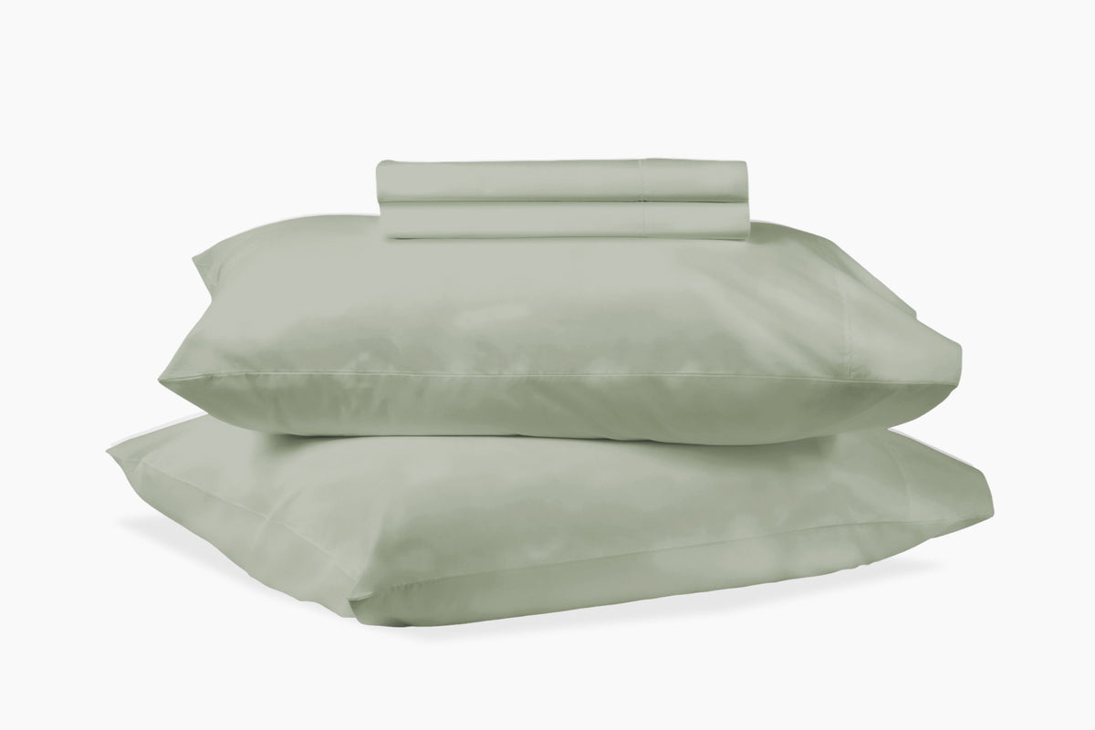 A stack of pillows and bed sheets, eucalyptus-green colorway, against a white background