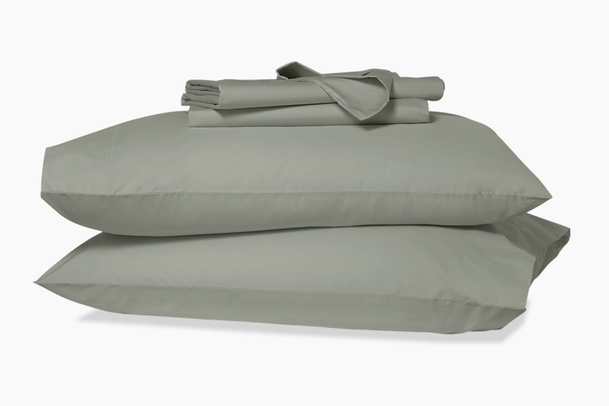 A stack of pillows and bed sheets, eucalyptus-green colorway, against a white background