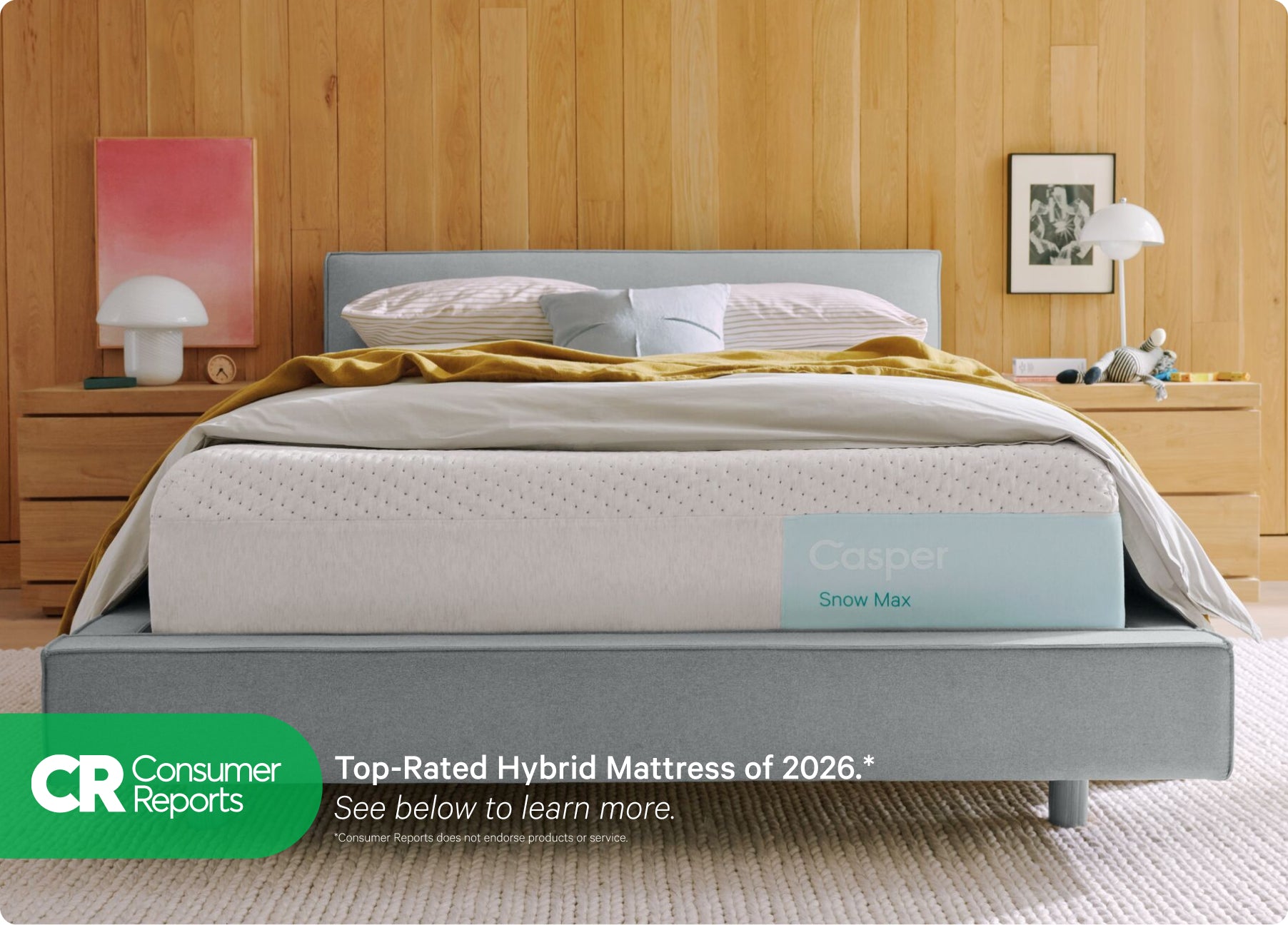 Front view of Casper's Snow Max mattress on a bed frame with pillows and a folded blanket on top. At the bottom of the image appears text that reads "Consumer Reports. Top rated hybrid mattress of 2026.* See below to learn more. *Consumer Reports does not endorse products or service."