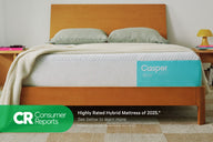 Front-view of the Casper Snow mattress in a bed frame with two pillows and a blanket folded on top. Beneath the image appears text which reads "Consumer Reports. Highly rated hybrid mattress of 2025.* See below to learn more. Consumer Reports does not endorse products or service."