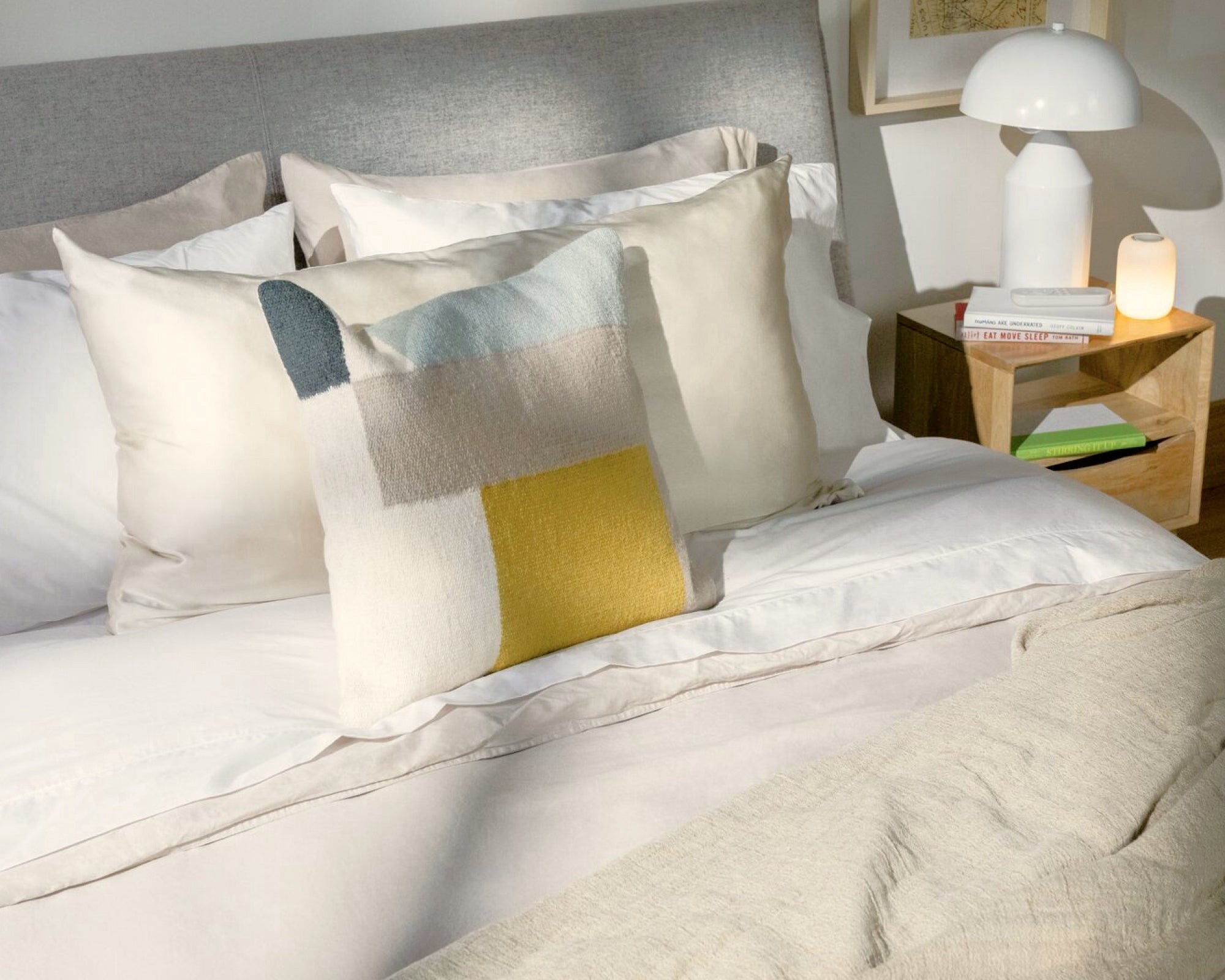 A fully made bed with several pillows, a duvet, sheet set, a blanket folded on top, and the mattress sits on top of a bed frame with a headboard.