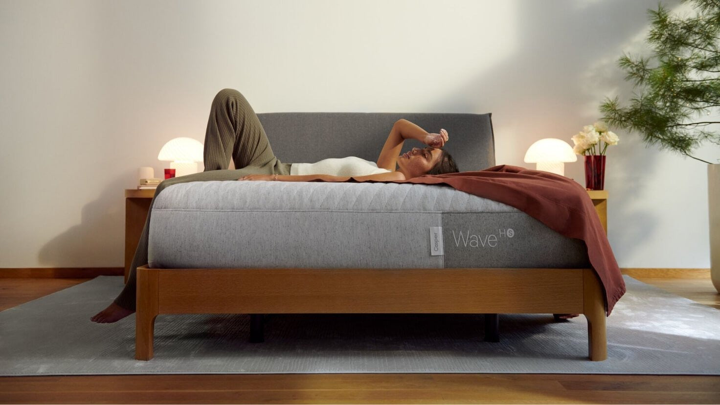 Front view of a woman lying on her back in bed. The mattress sits on top of a wooden Repose Bed Frame