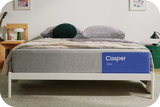 The One mattress on a bed frame with a blanket and pillows on top of it in a bedroom setting