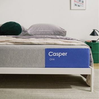 The One mattress on a bed frame with a blanket and pillows on top of it in a bedroom setting