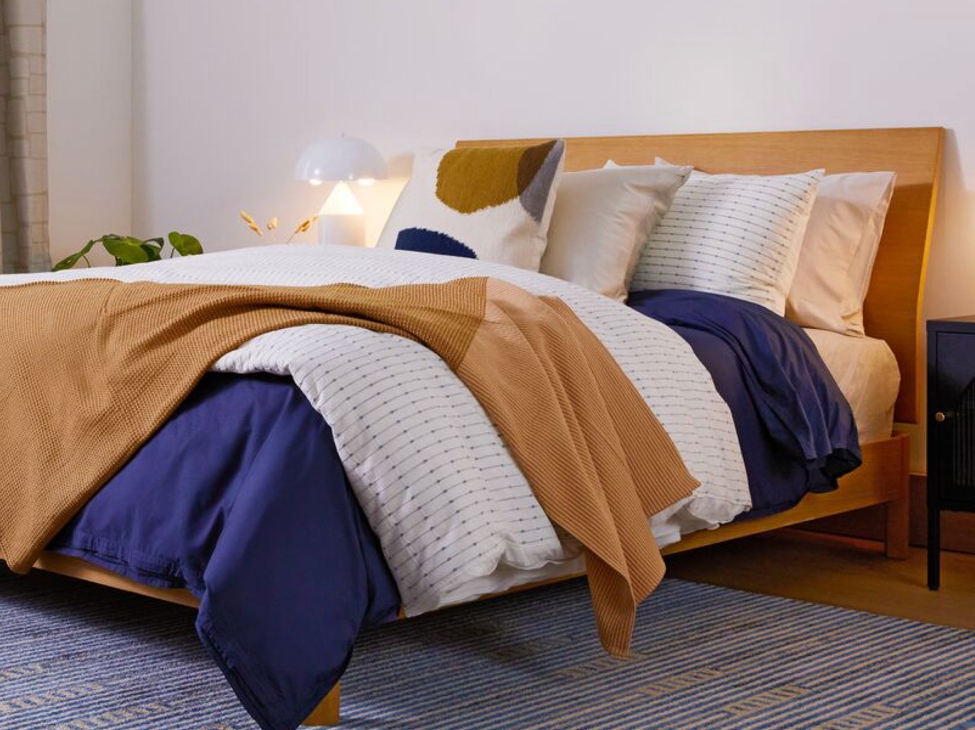 Image of a fully made bed from a front-side angle. It has several pillows placed neatly against the headboard, two comforters, and a folded throw blanket on top of them.