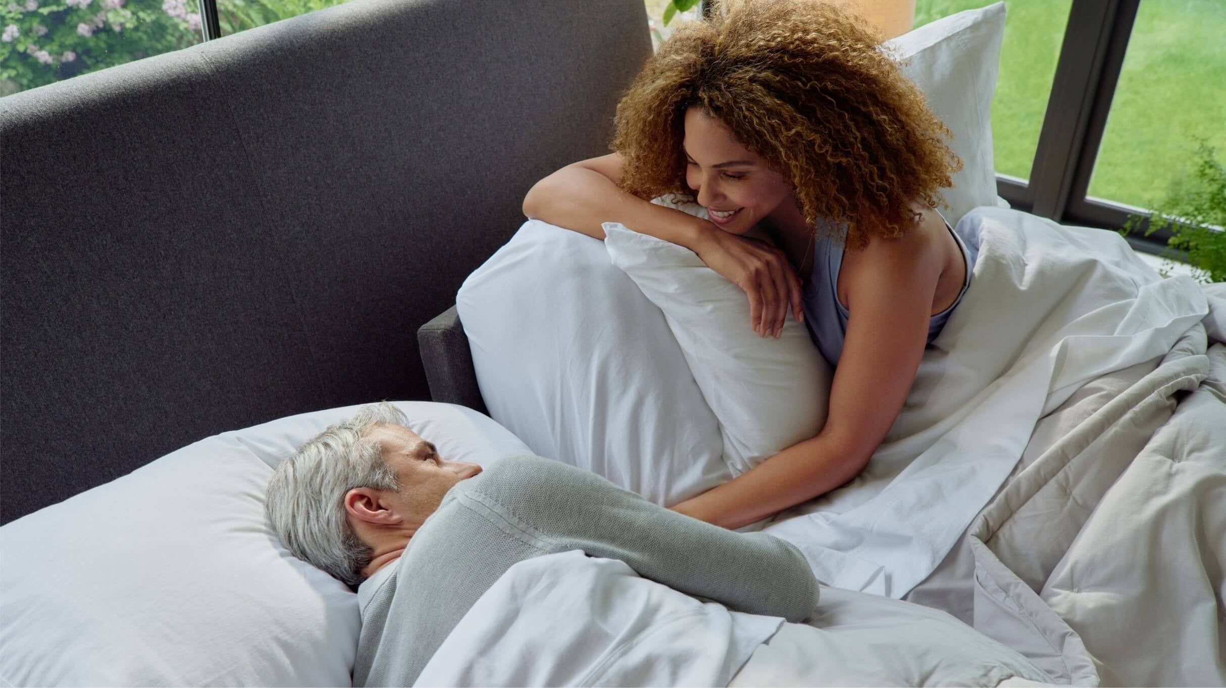 A couple lies awake in bed on a split king sized adjustable base. One of their halves is flat while the other's has a raised head lift for customized comfort.