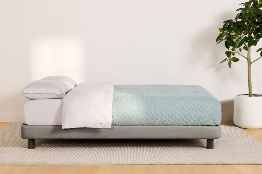 Side view of a fully made bed. The mattress sits atop Casper's Upholstered Bed Frame, gray color.