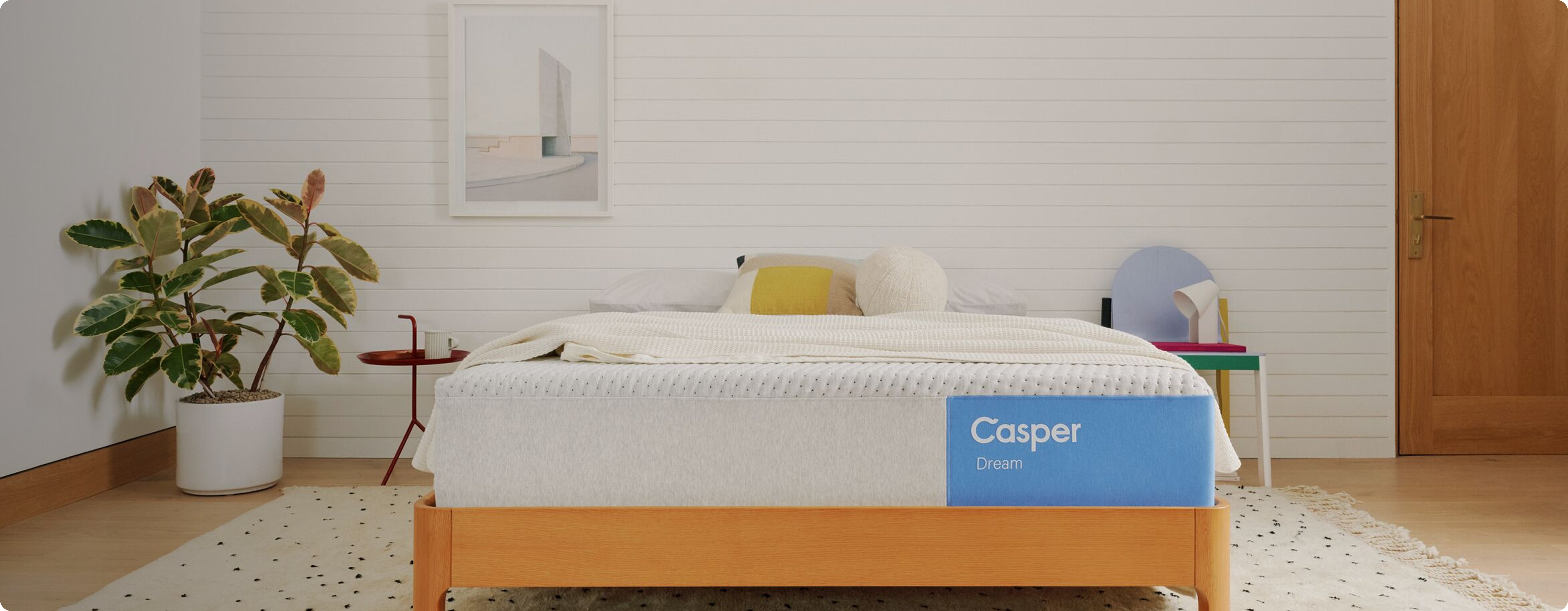 Casper mattress in a bedroom setting with a plant and side table.