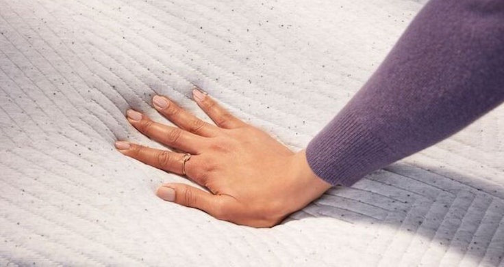 Close-up image of a person's hand pressing down on a mattress to feel it.