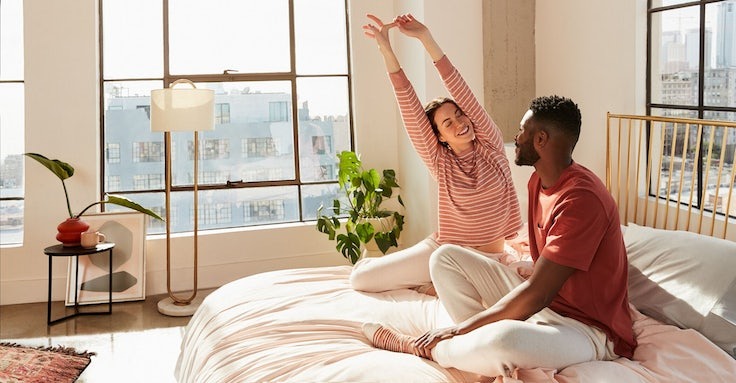 A couple sitting up on their bed and stretching.