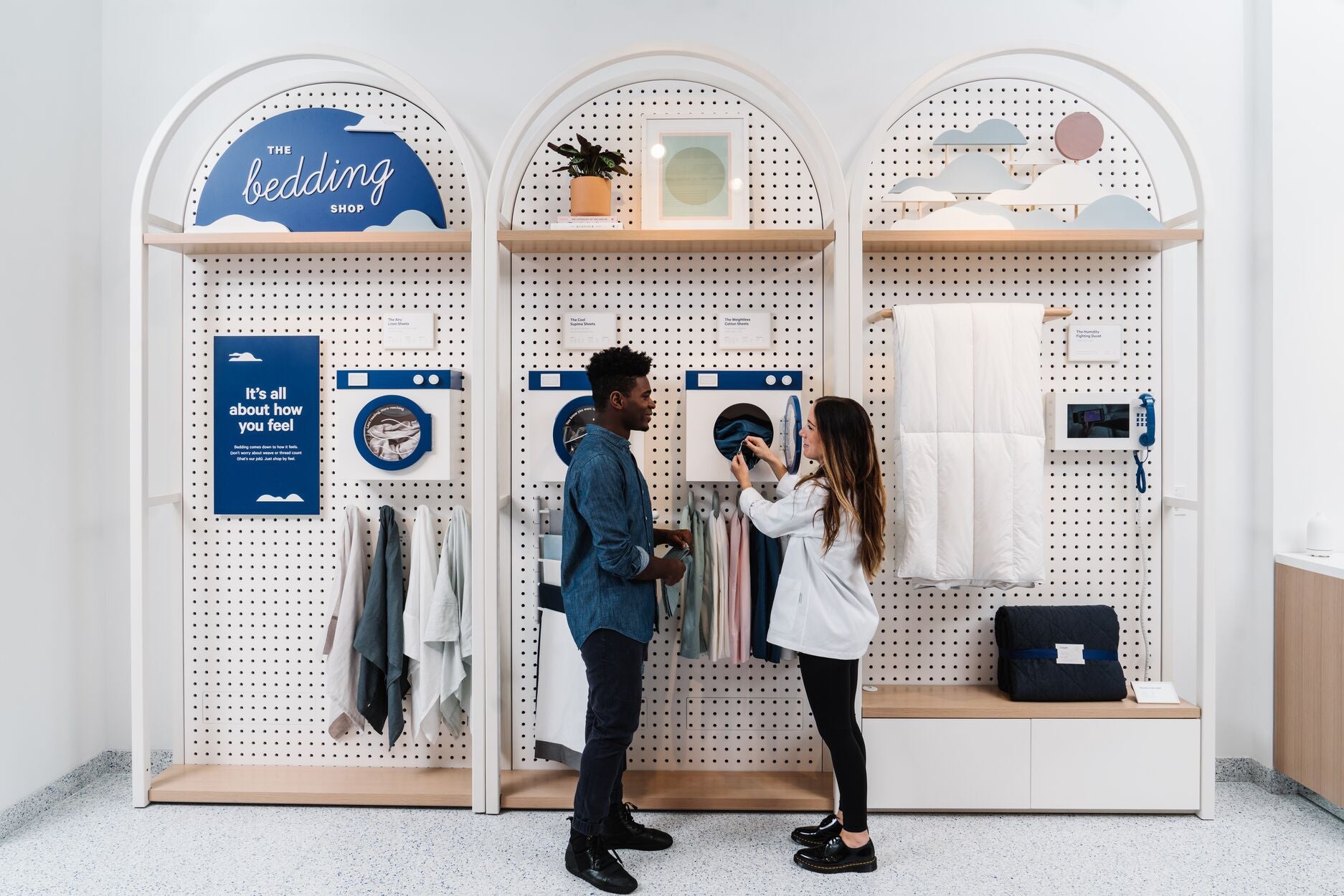A Casper retail store associate helps a customer look through products in the store. Behind them are various products hung up on the wall.