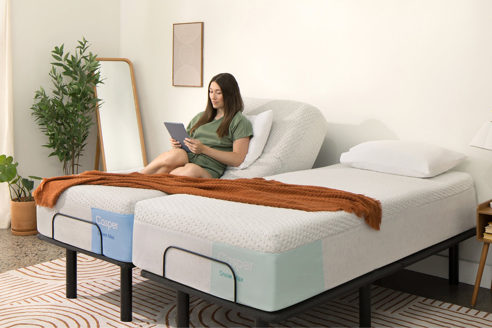 Lifestyle photo of a Split King sized Adjustable Base. The right mattress is lying flat while the head of the left mattress is raised to support a person reading in an upright position.