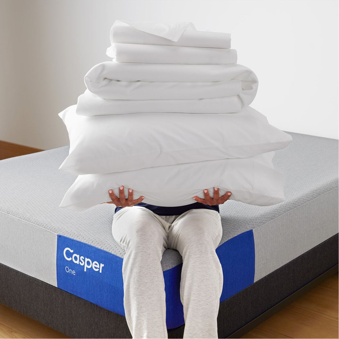 Person sitting on a Casper mattress with folded white bedding stacked above them