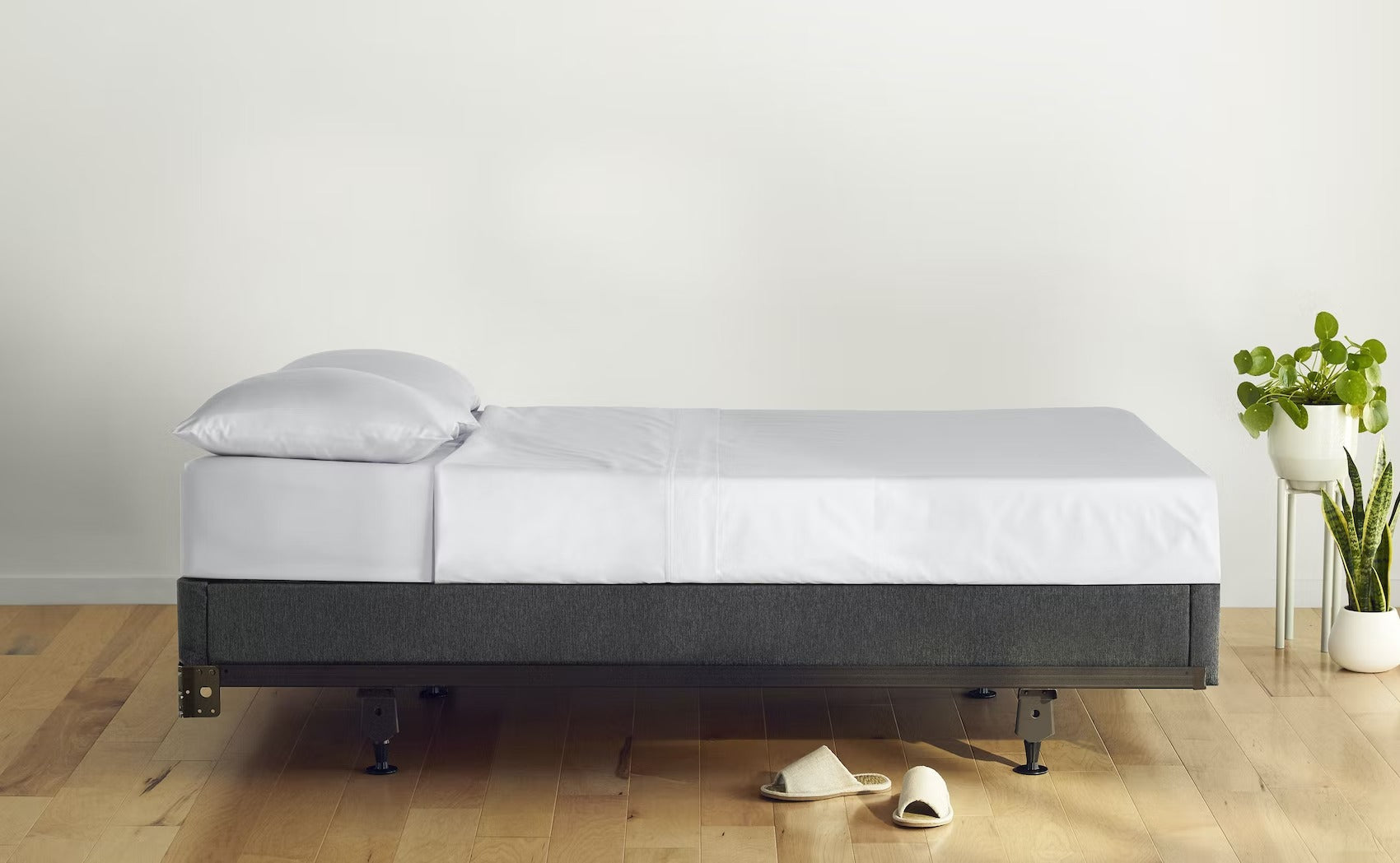 Side image of a bed against an empty wall. The bed is made with pillows and a sheet set. The mattress sits on top of Casper's Foundation, which is placed on a metal bed frame on a wooden floor.