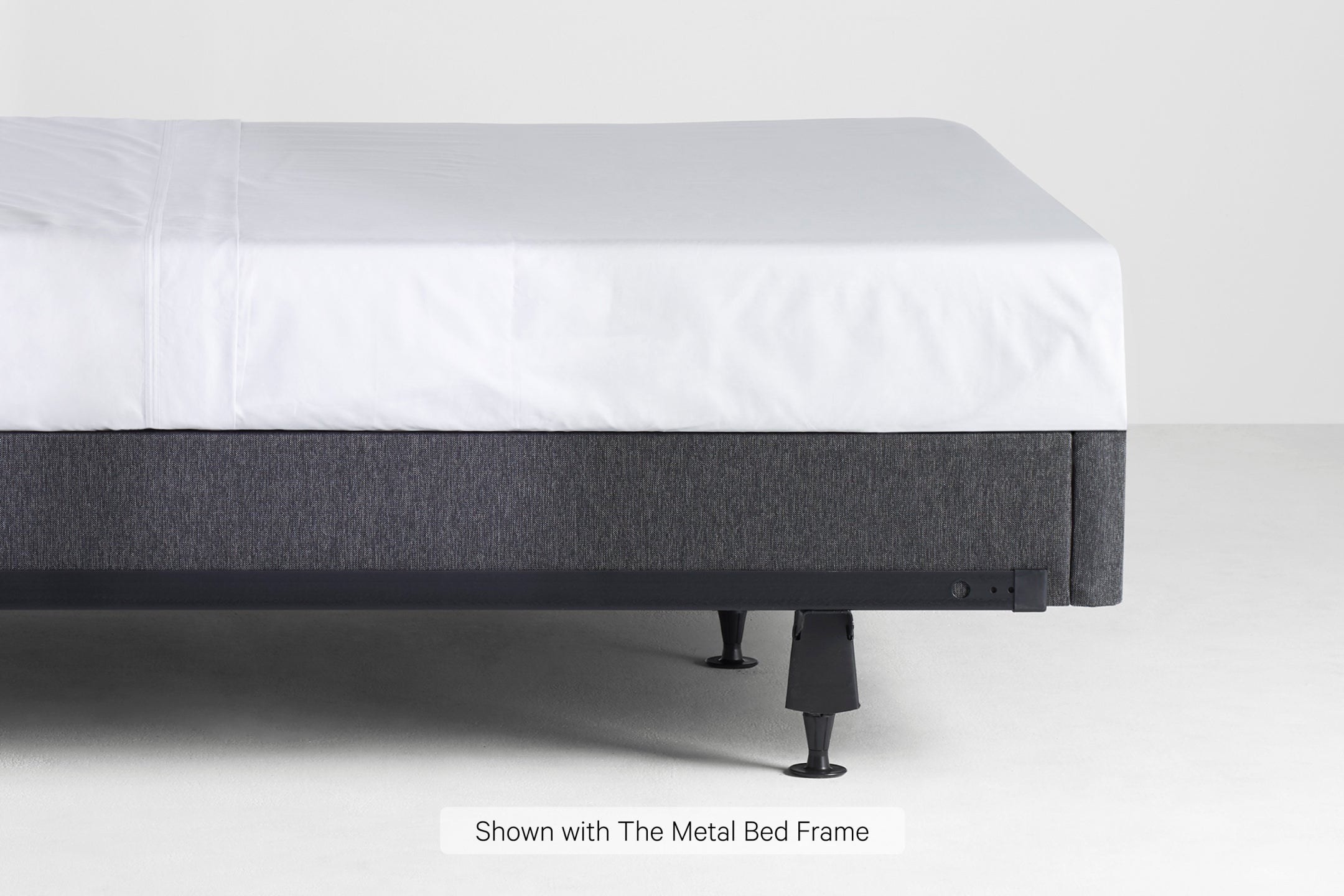 Side view of the bottom half of a made bed. The mattress is on a Foundation on top of a metal bed frame