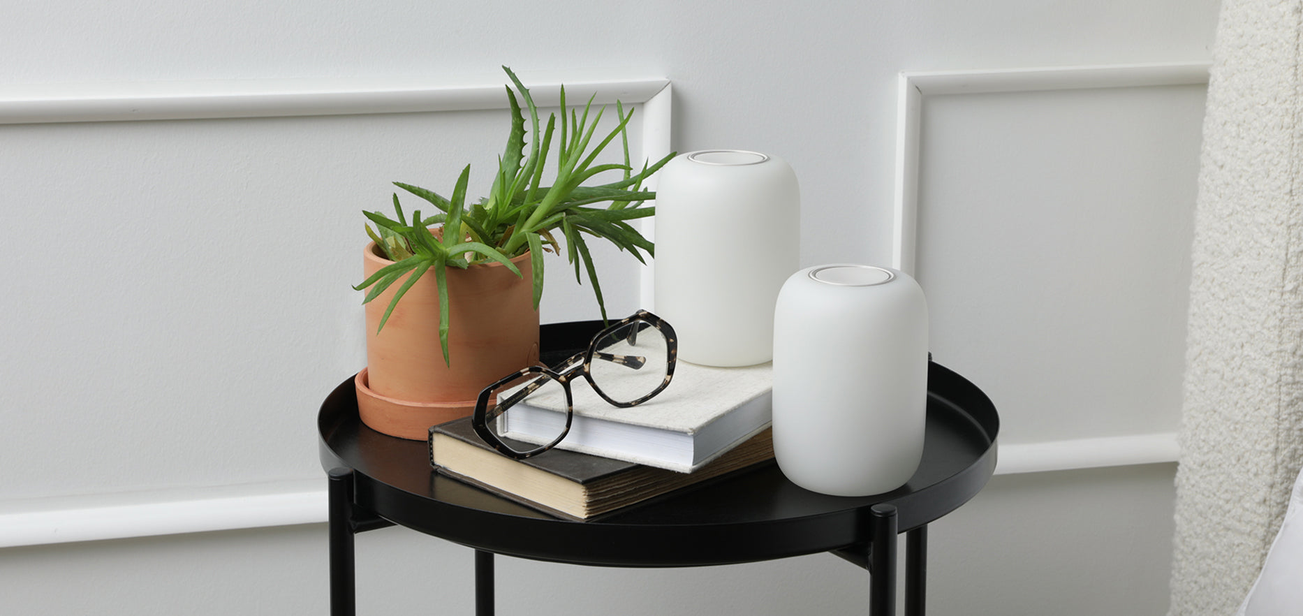 Lights-on image of two glow lights sitting on a night table with books and a plant